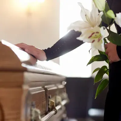 A hand resting on a casket beside white lilies